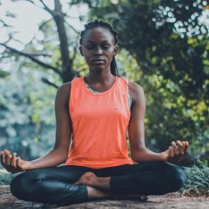 A woman meditating peacefully outdoors in a lush green setting, promoting relaxation and mindfulness.